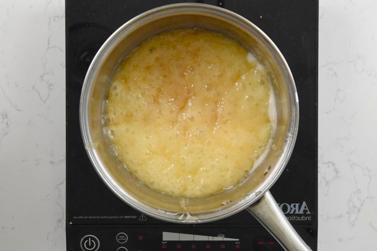 A saucepan filled with bubbling churro caramel sauce is placed on a black induction stove. The light golden brown caramel indicates its cooking to perfect churro toffee sweetness. The stove features touch controls with digital displays, ensuring precise heat for this delightful treat.