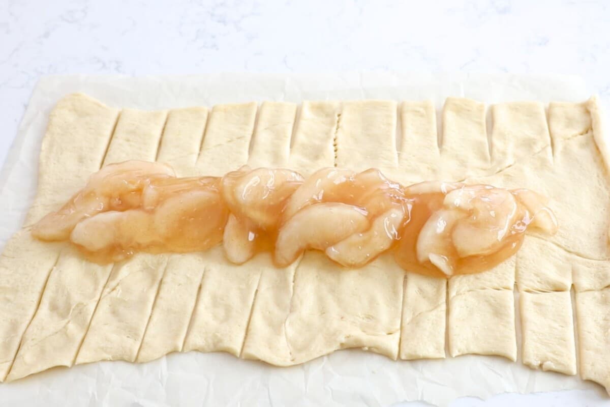 crescent roll sheet rolled out on counter with slits and apple pie filling down the middle.