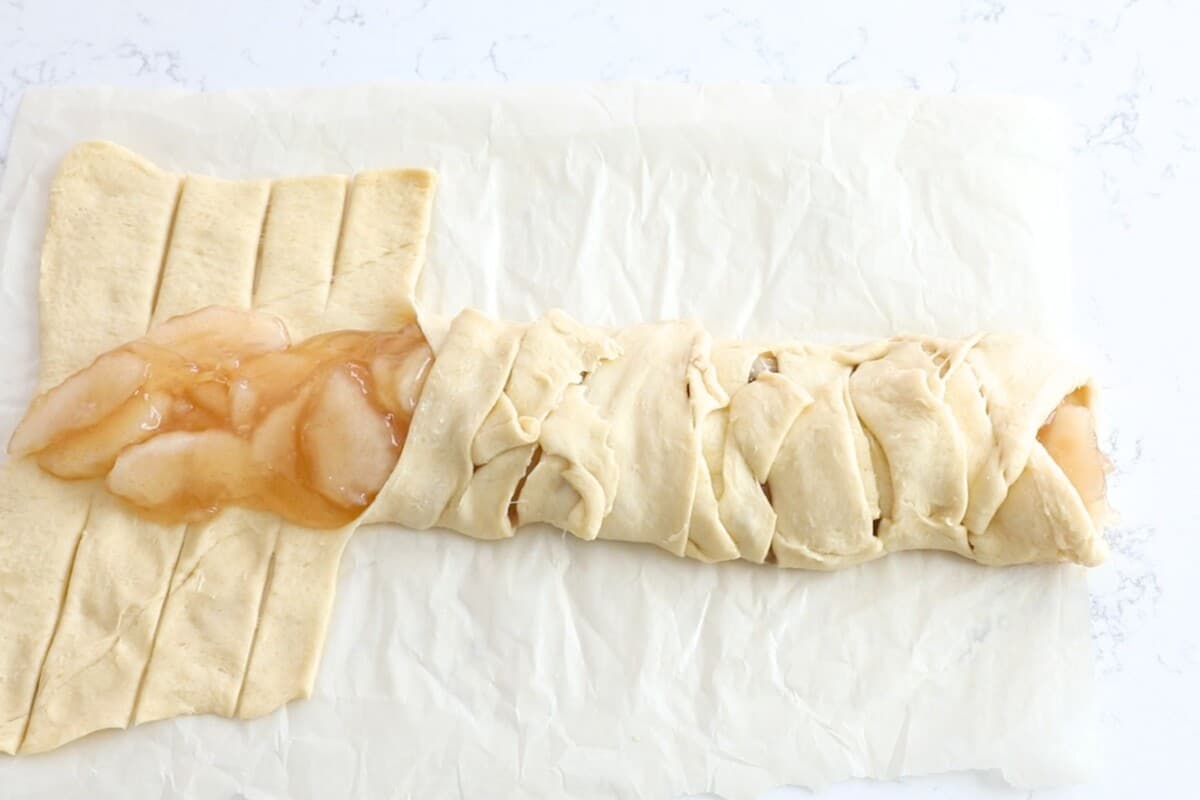 crescent roll sheet rolled out on counter with apple pie filling  starting to be wrapped up like a braided danish.