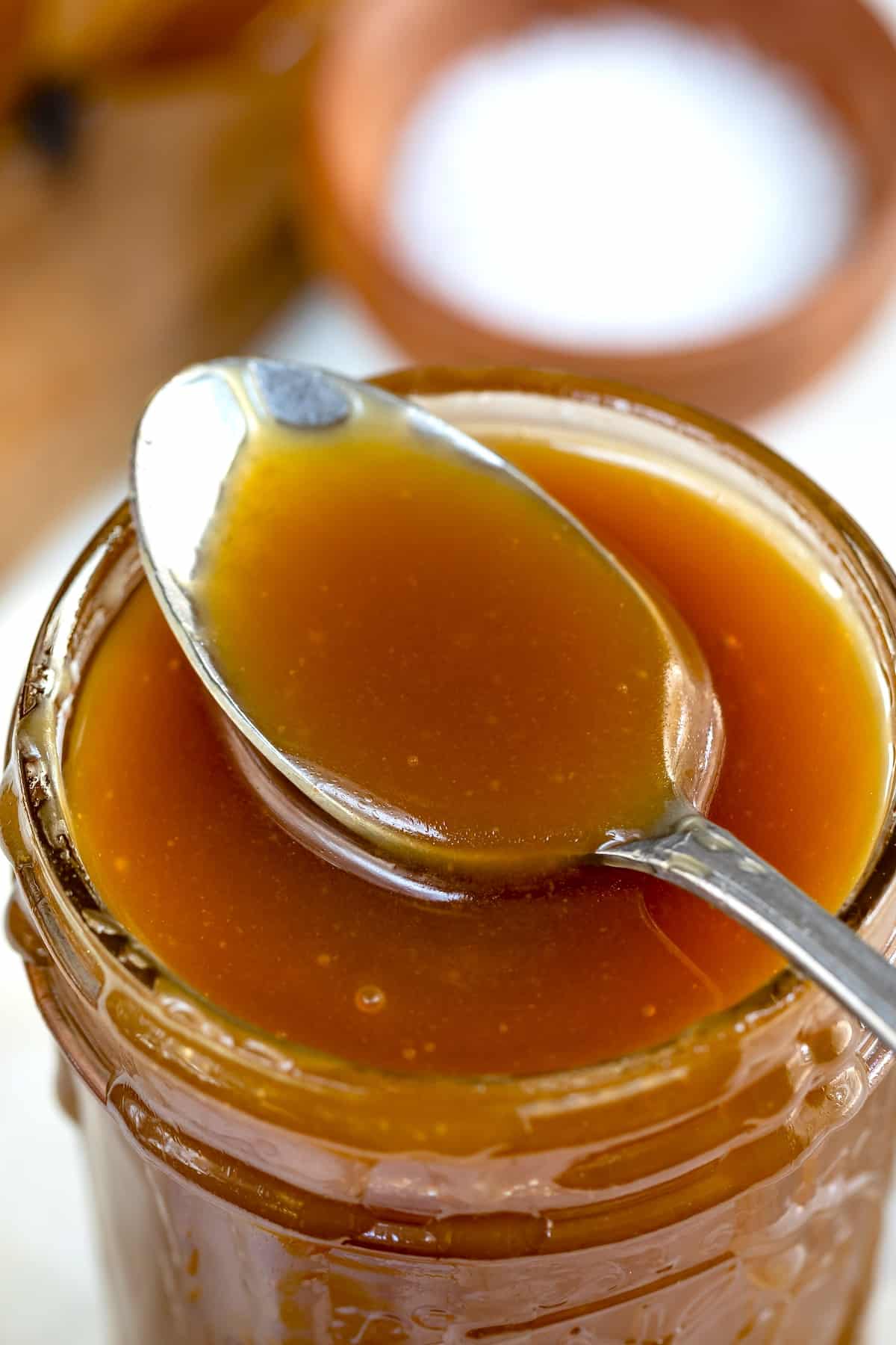 spoon with caramel resting on open jar of caramel.