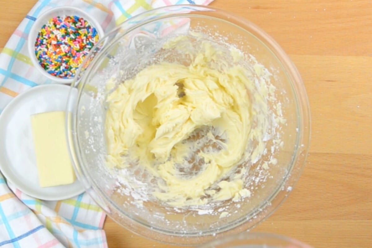 creamed butter and sugar in a clear bowl on brown table with sprinkles next to it.