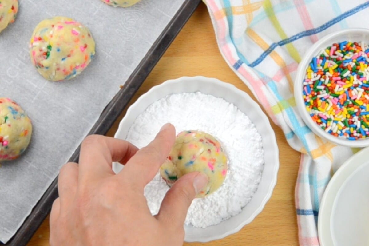 hand dipping cookie in powdered sugar.