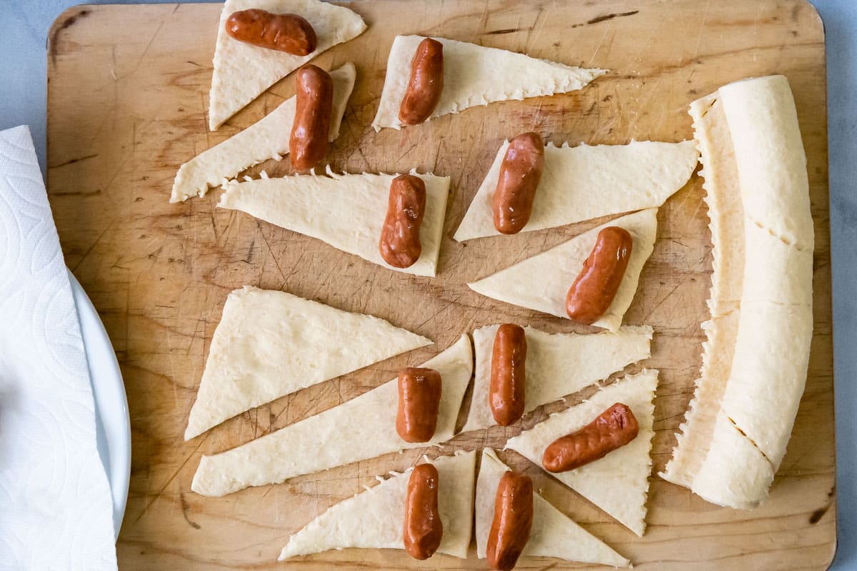 crescent rolls cut into triangles and spread out on cutting board with lil' smokies on top.