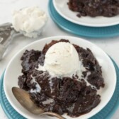 Slow cooker brownie pudding on a blue plate with a scoop of ice cream on top