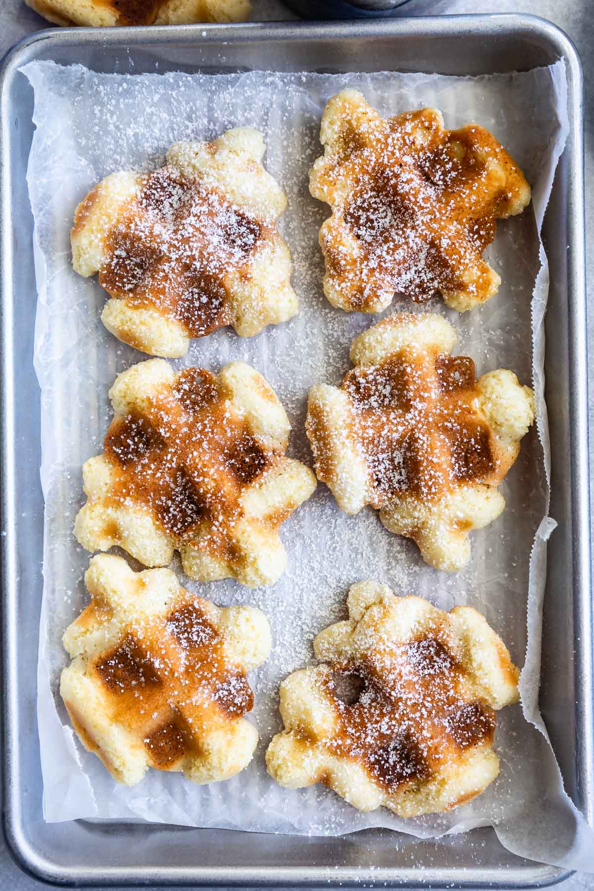Overhead view of six waffle cookies sprinkled with powdered sugar on a baking sheet