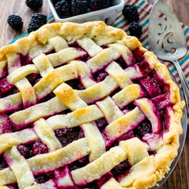 pie with lattice top with blackberries behind on wood surface