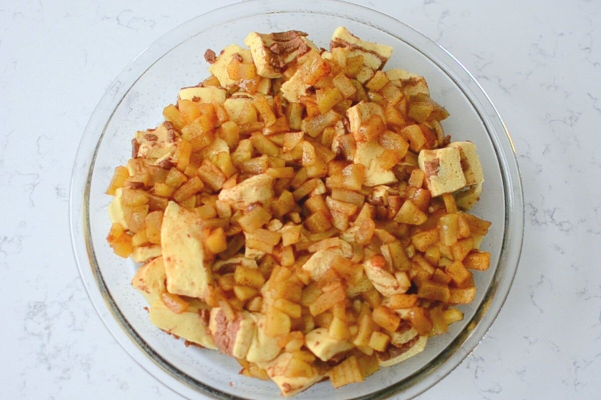 casserole with apples and chopped up cinnamon rolls in pie plate.