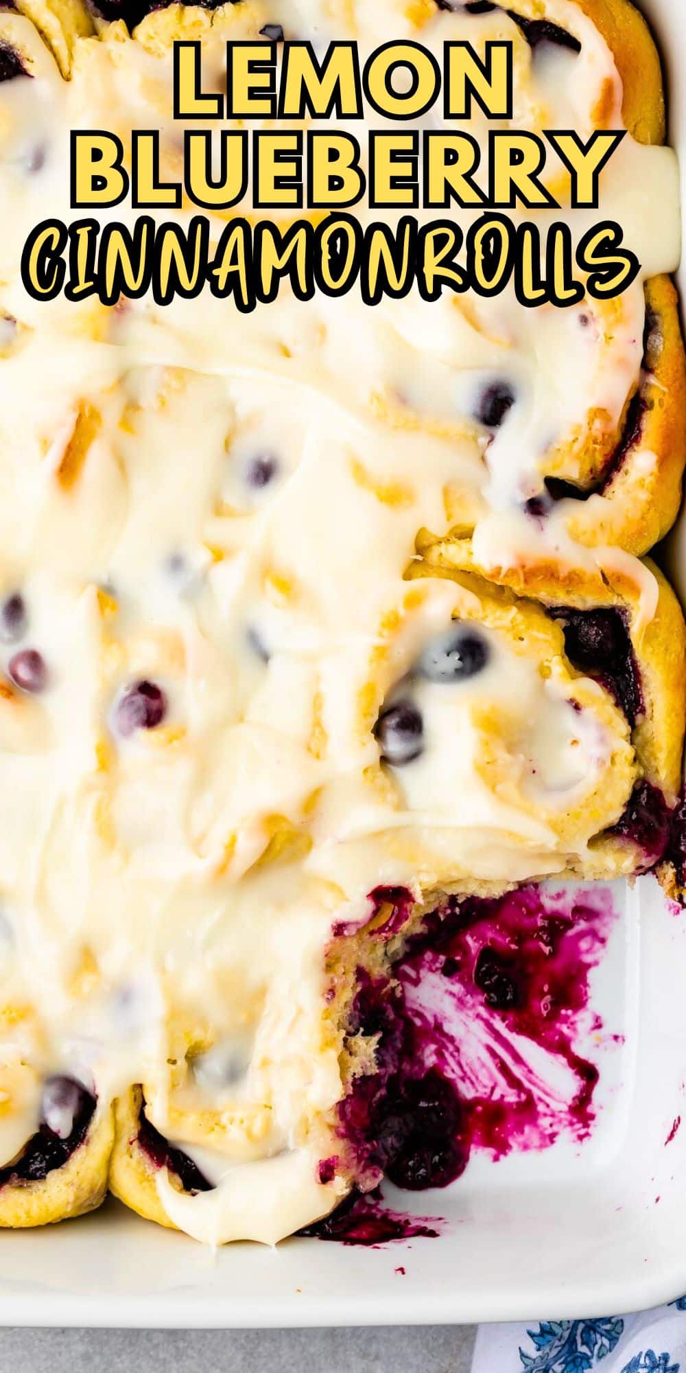 A tray of blueberry sweet rolls topped with icing tempts from the counter. One roll is missing, revealing a juicy blueberry filling. Text at the top reads LEMON BLUEBERRY CINNAMON ROLLS.