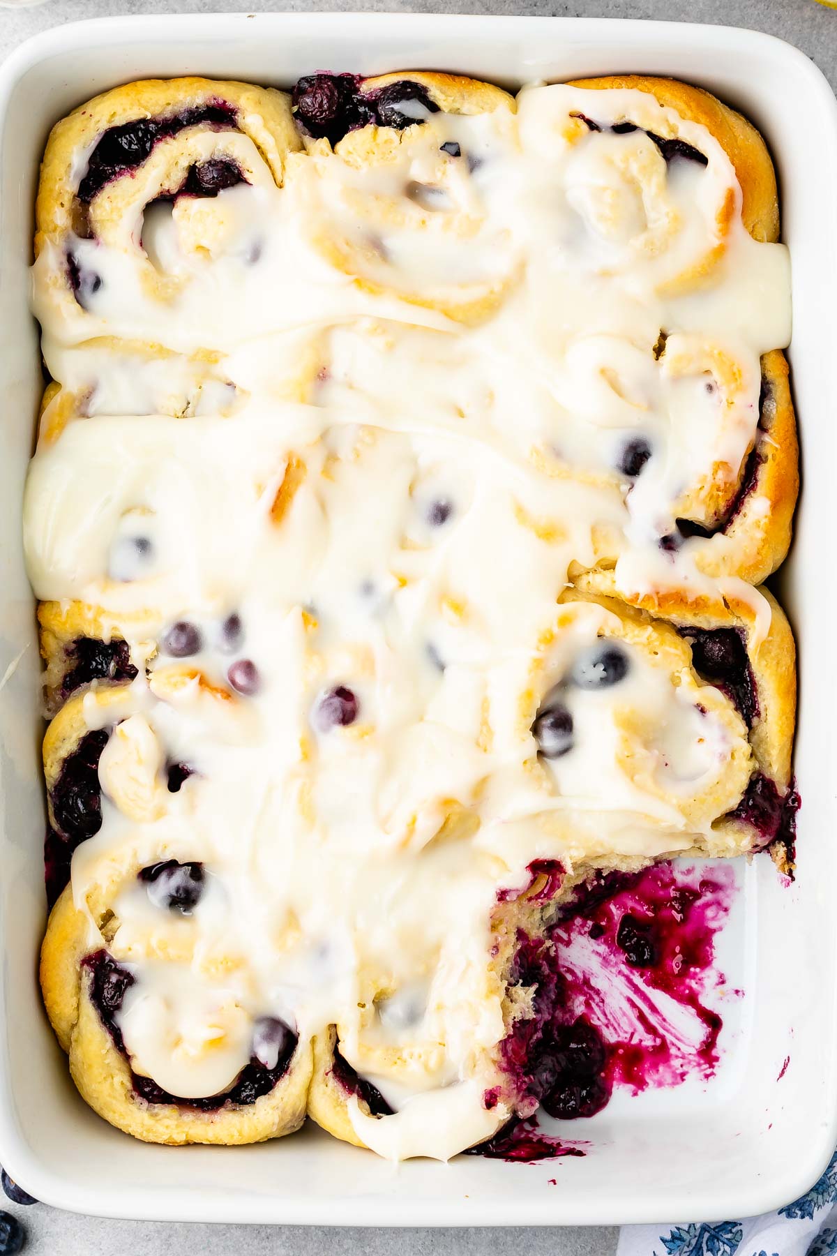 overhead shot of blueberry cinnamon rolls with one missing and lemon glaze