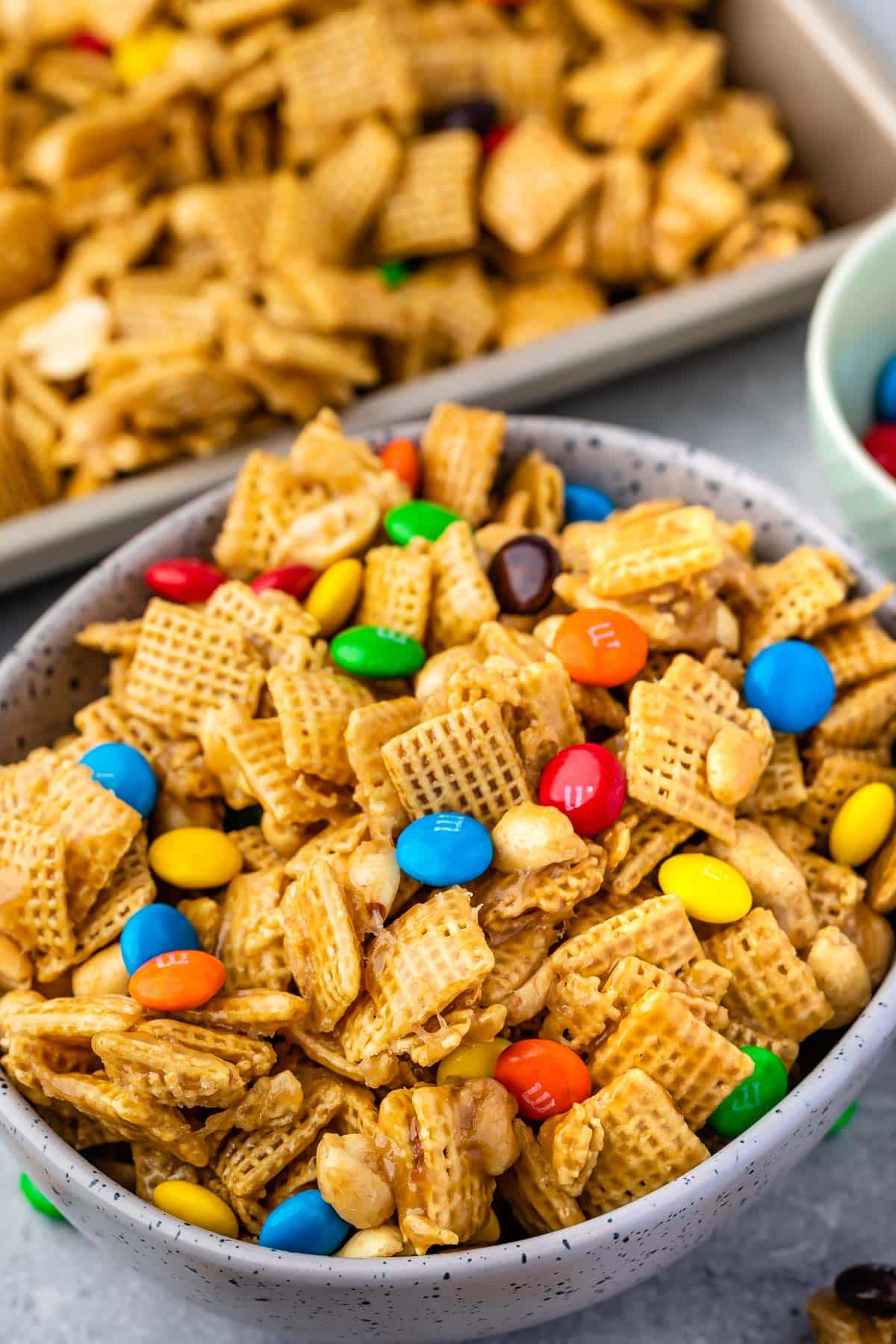 bowl of Chex mix with M&Ms with pan of mix behind