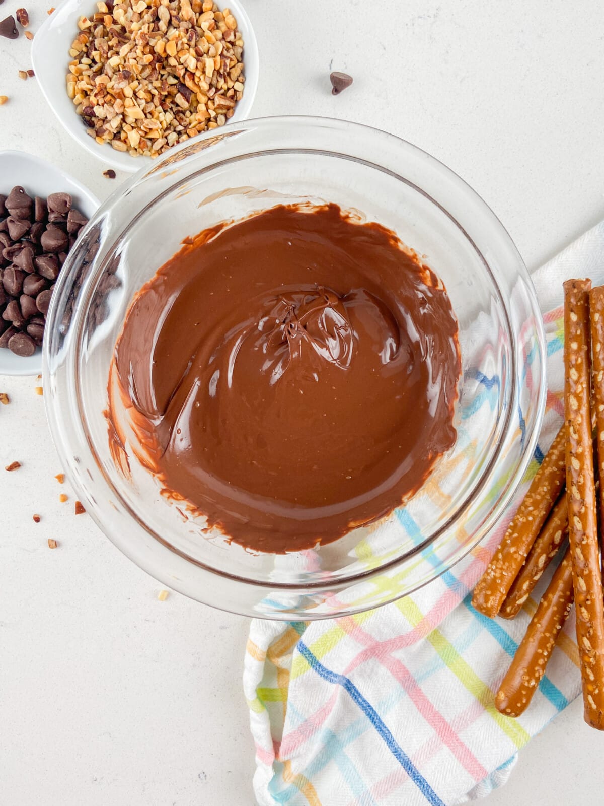 bowl of melted chocolate with nuts and pretzels around.