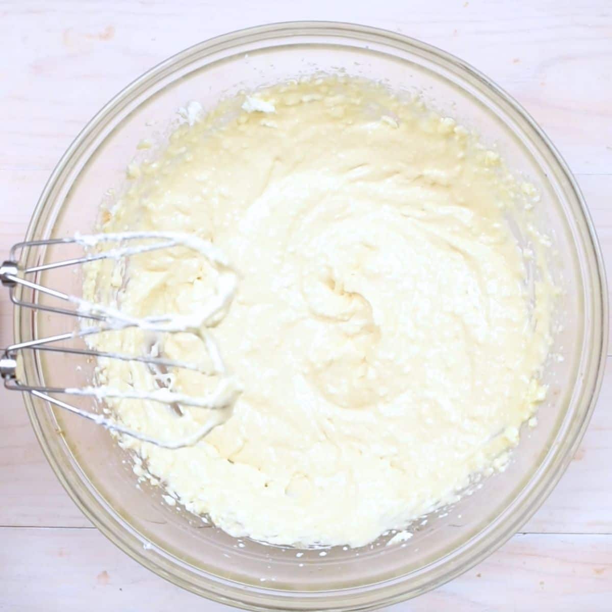 cheesecake batter in clear bowl with mixer beaters.