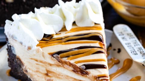 cheesecake with peanut butter and chocolate sauce drizzled over it and whipped cream on the edge.