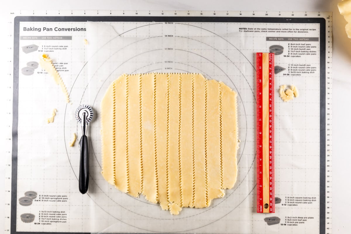 pie dough on work surface cut into strips with ruler and pie cutter next to it.