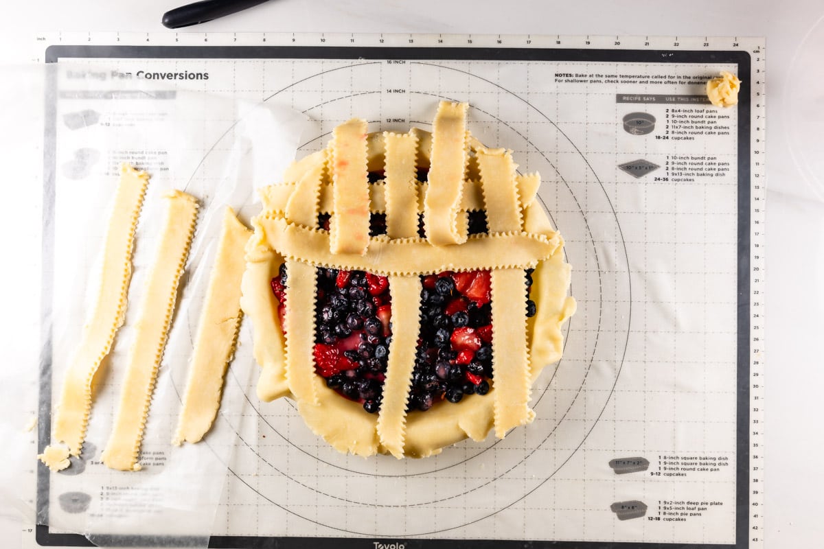 pie with fruit filling topped with vertical strips of pie dough - every other one is folded up and one strip is horizontal across.