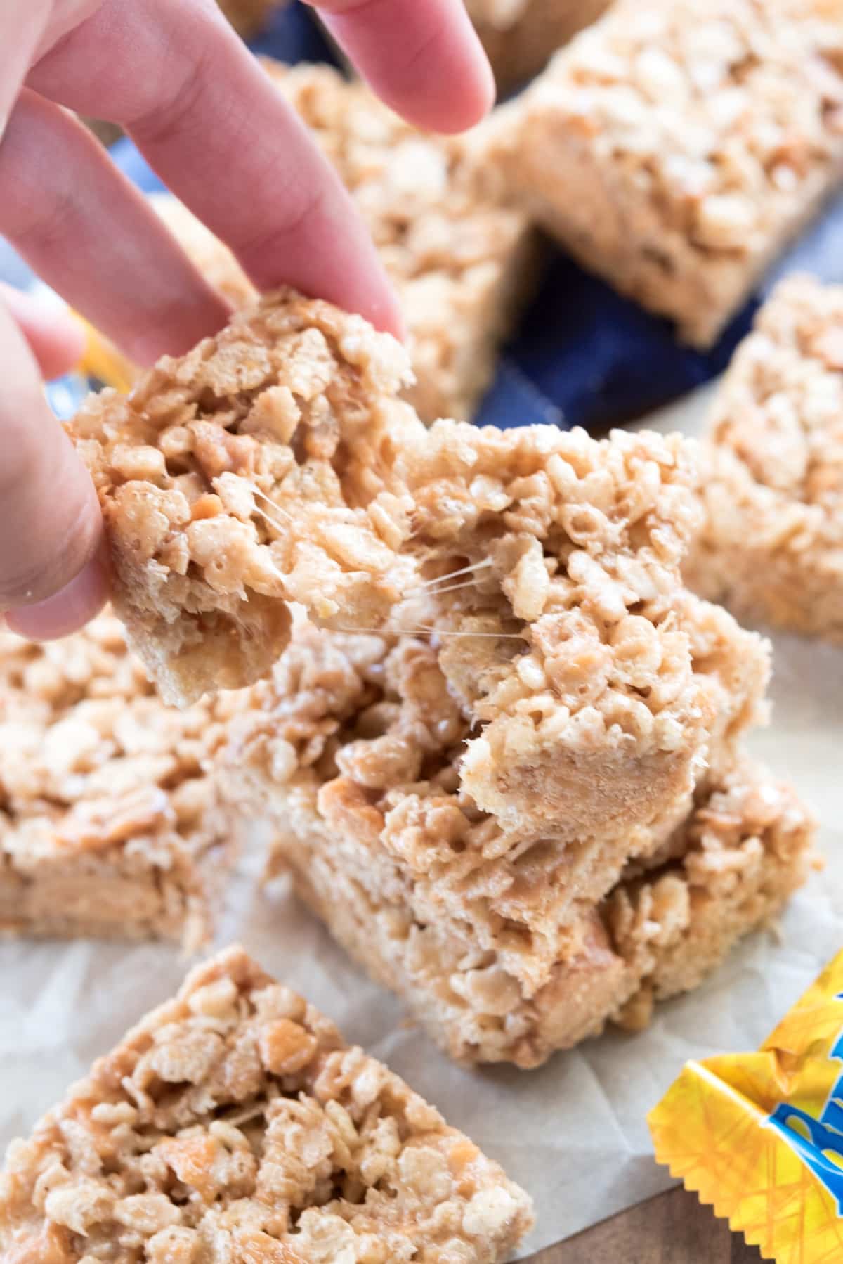 hand holding stacked Rice Krispie treats with butterfingers spread around.