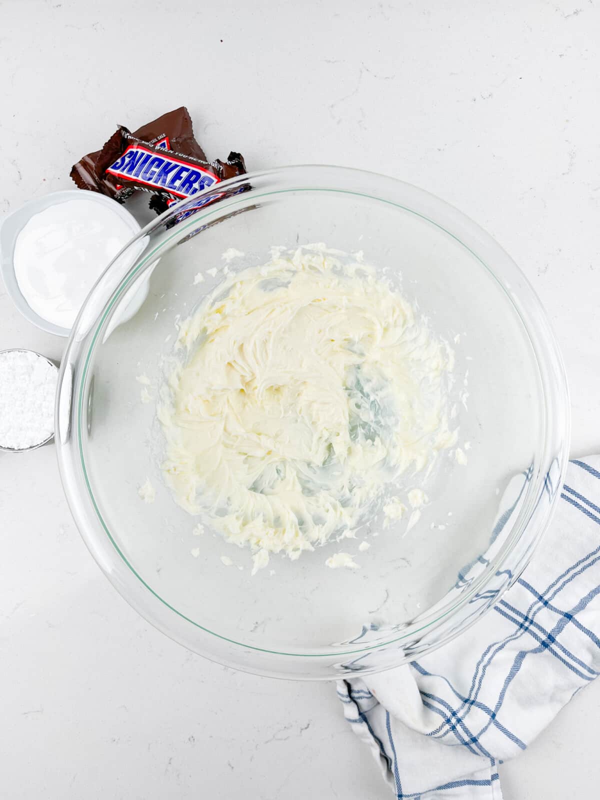 process shot of snickers dip being made on a white marble counter.