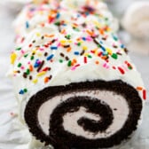 chocolate cake roll covered in white frosting and colorful sprinkles.