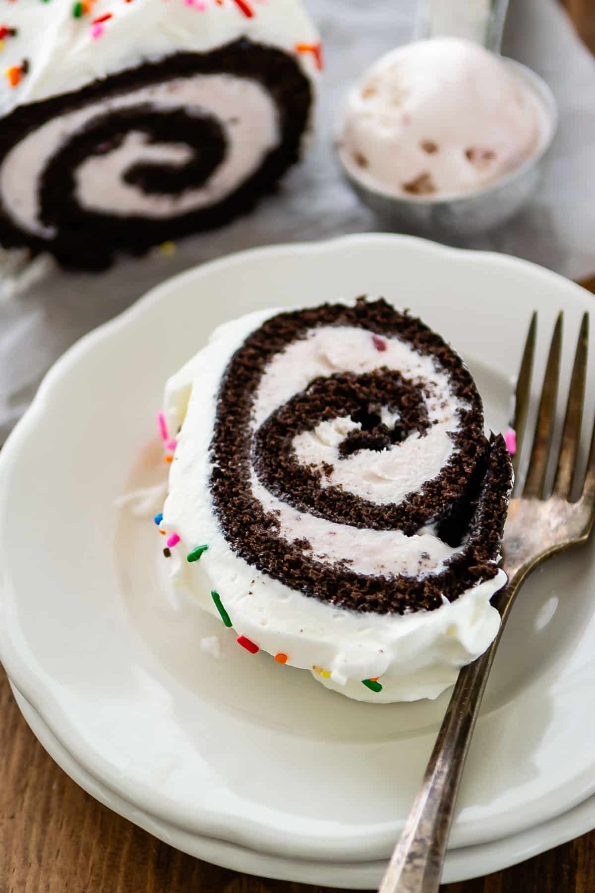 chocolate cake roll covered in white frosting and colorful sprinkles.