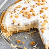 peanut butter pie in a glass pie plate with peanuts on top.