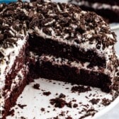 brown layered cake with white frosting and crushed oreos on top.