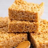 stacked Rice Krispie treats next to a spoonful of peanut butter.