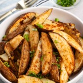 potato wedges in a white bowl with a green garnish.