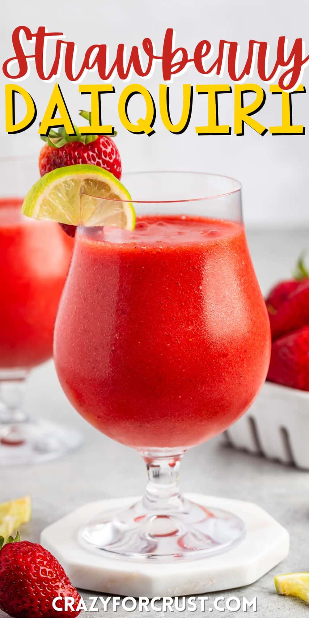 strawberry daiquiri in a stout clear glass with lemon and strawberries around and on the rim with words on the image.