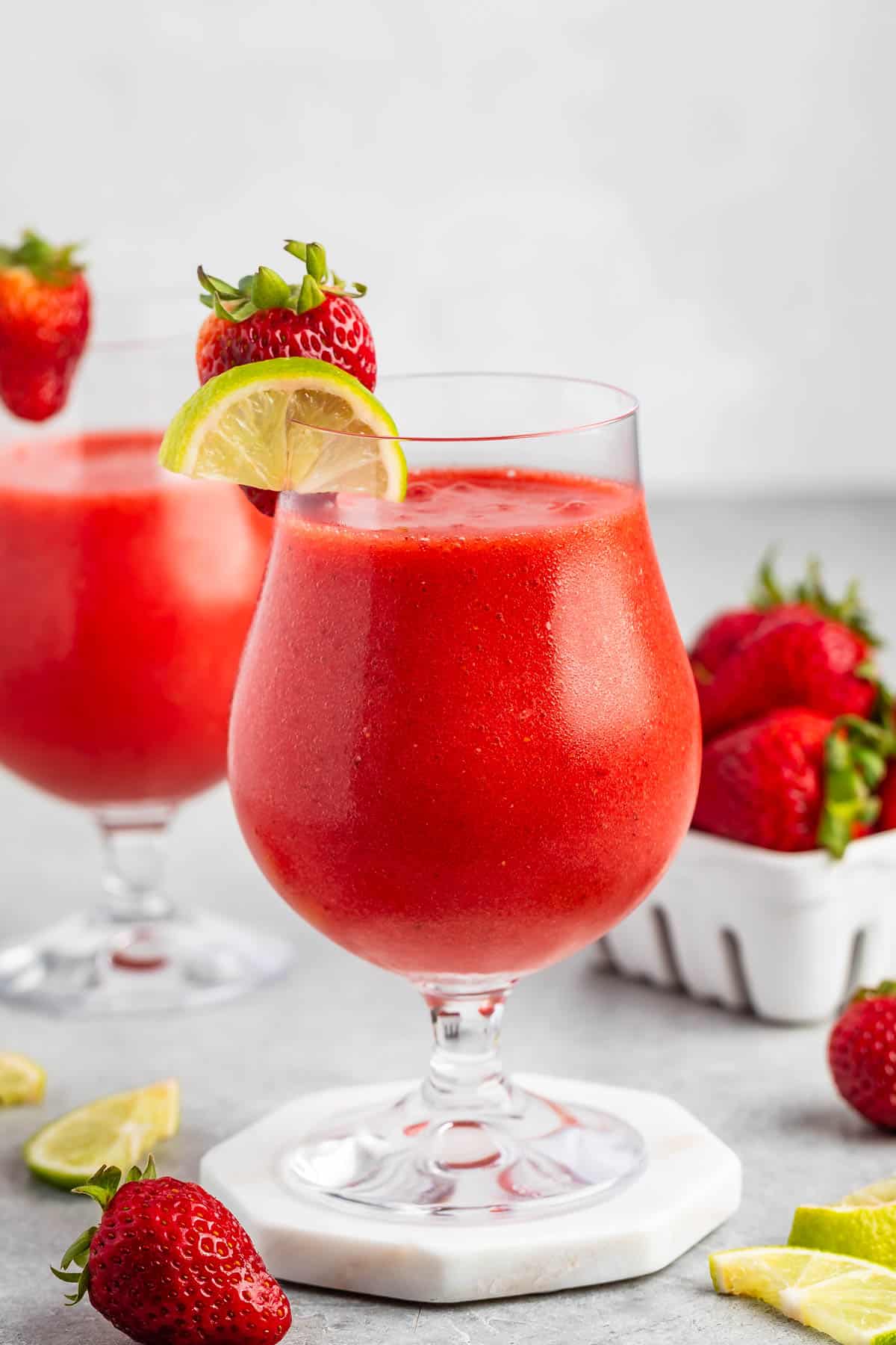 strawberry daiquiri in a stout clear glass with lemon and strawberries around and on the rim.