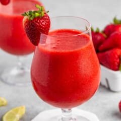 strawberry daiquiri in a stout clear glass with lemon and strawberries around and on the rim.