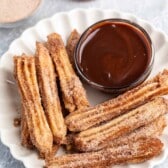 churros covered in cinnamon sugar on a white plate next to chocolate.