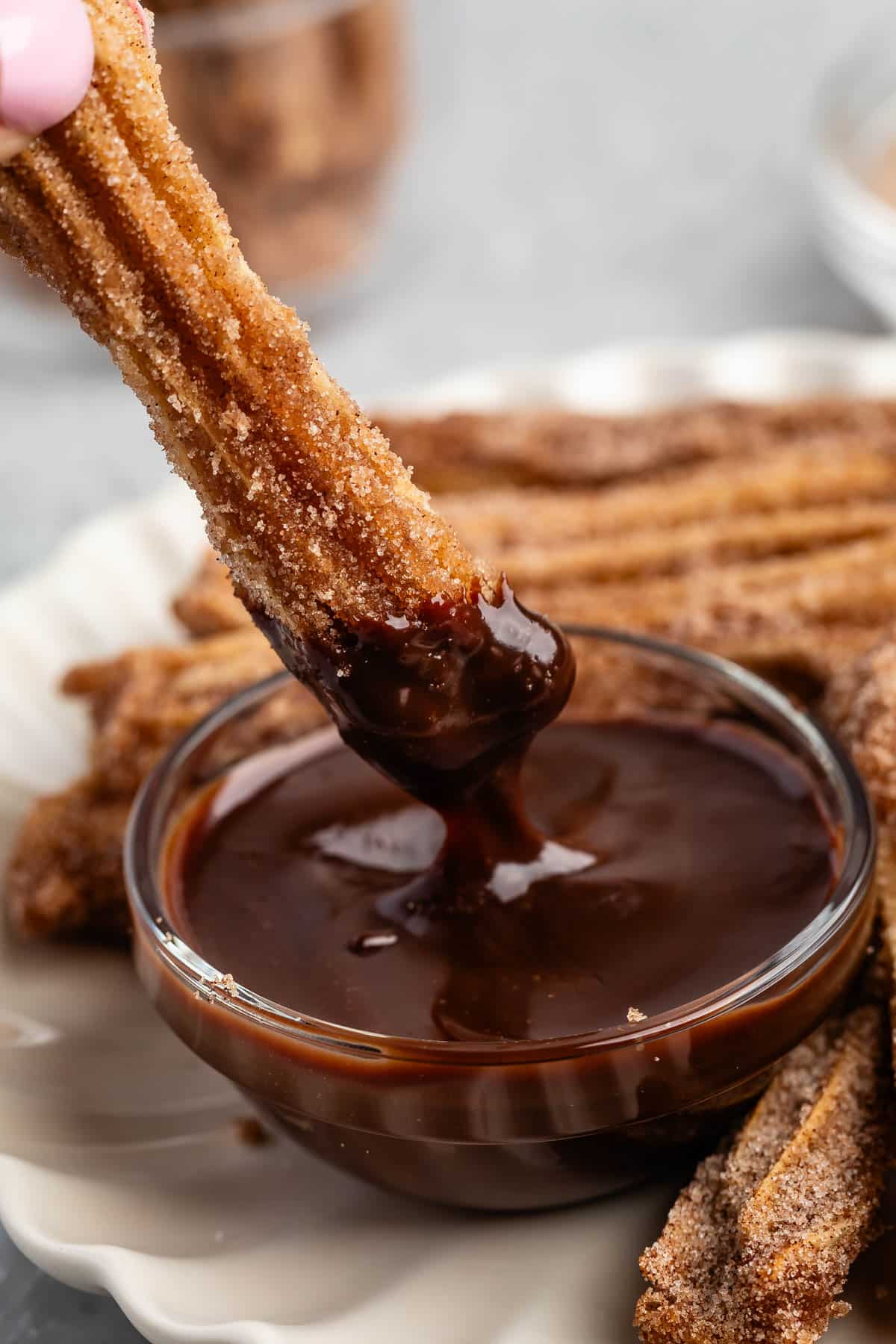 hand dipping a churro in chocolate sauce.