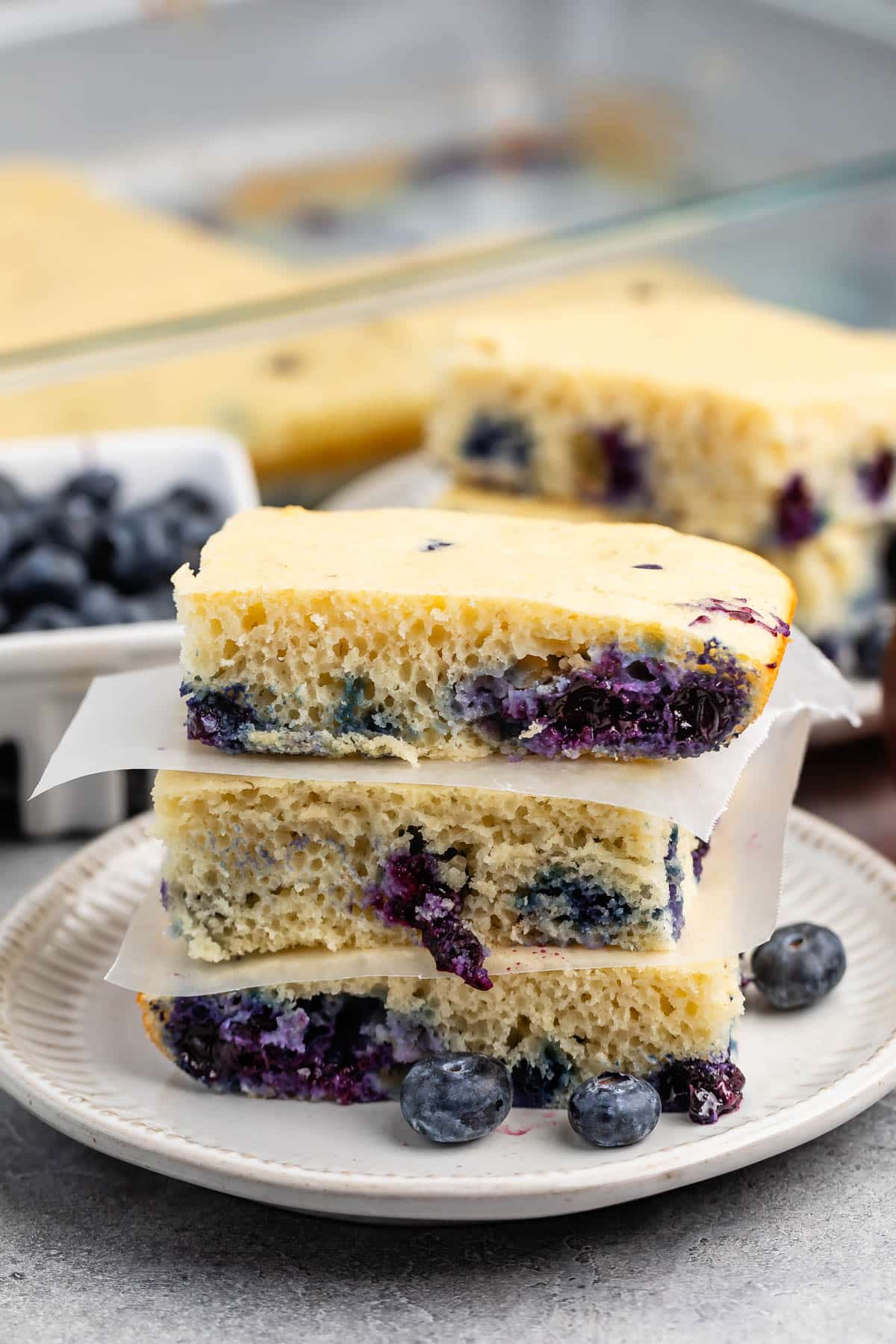 stacked square pancakes with blueberries baked in on a white plate.