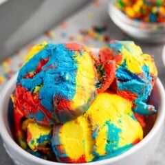 many scoops of red and yellow and blue ice cream mixed in a white bowl.