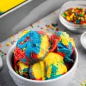 many scoops of red and yellow and blue ice cream mixed in a white bowl.