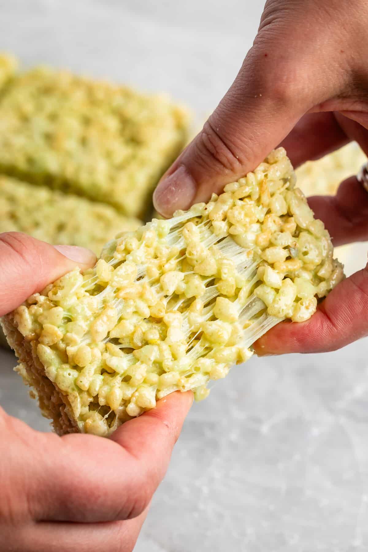 two hands pulling the pistachio Rice Krispie treats apart.