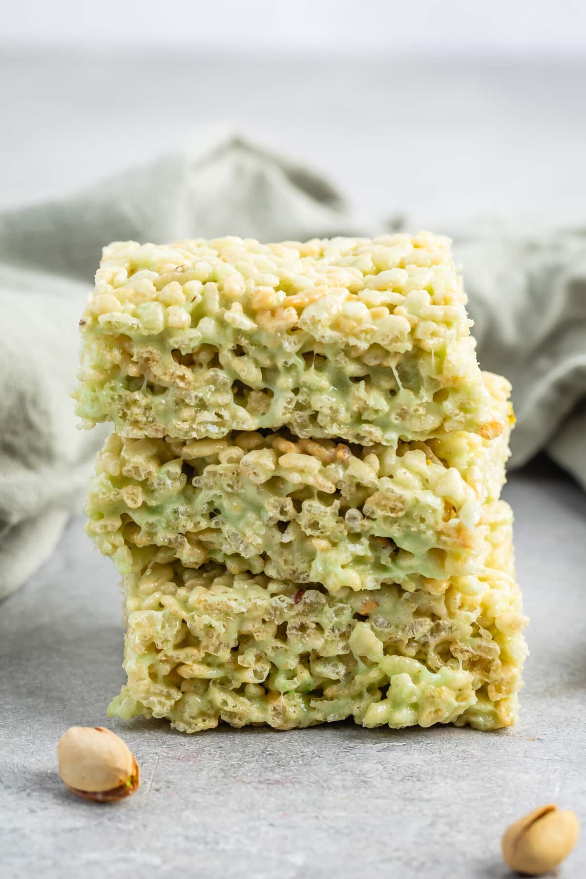 stacked green Rice Krispie treats on a grey table.