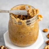 walnut butter in a clear jar with a spoon scooping it out.