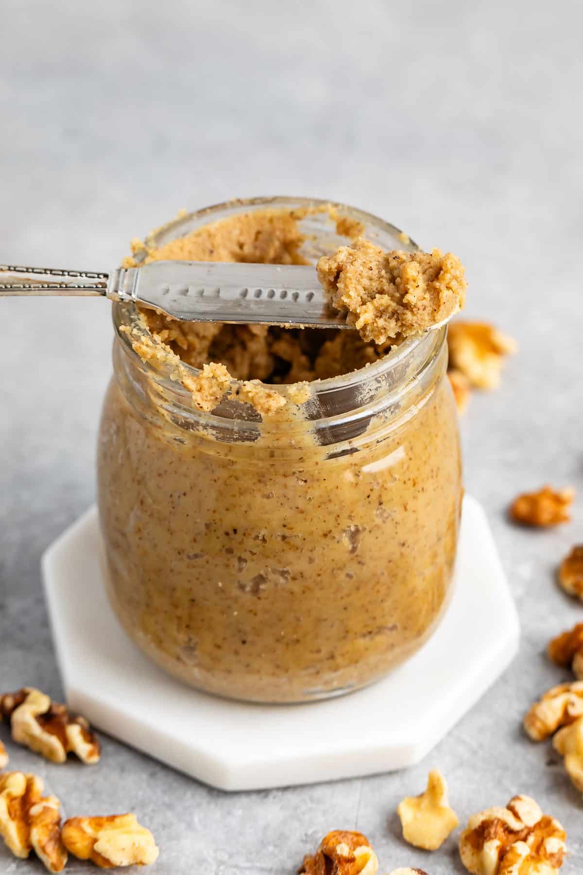 walnut butter in a clear jar with a spoon scooping it out.