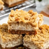 stacked apple cheesecake bars on a grey plate with a crumble topping.