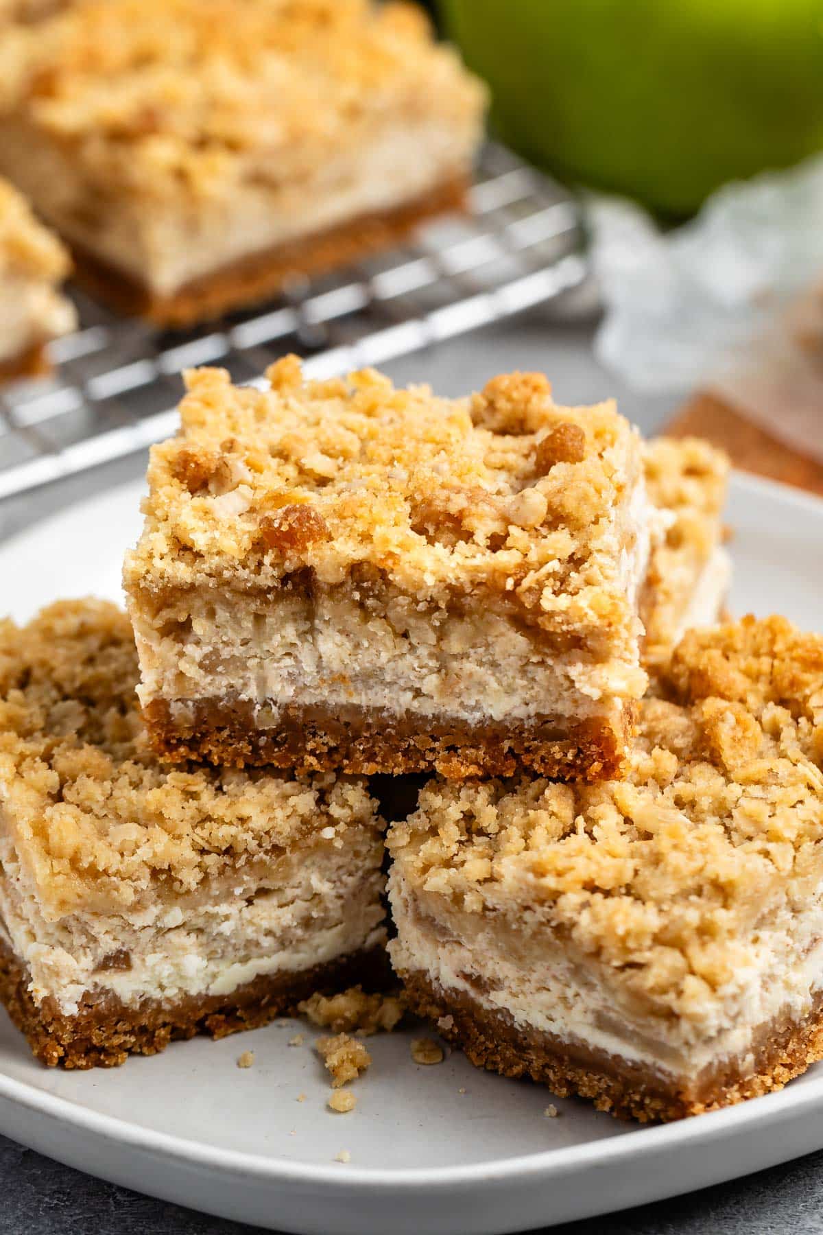 stacked apple cheesecake bars on a grey plate with a crumble topping.