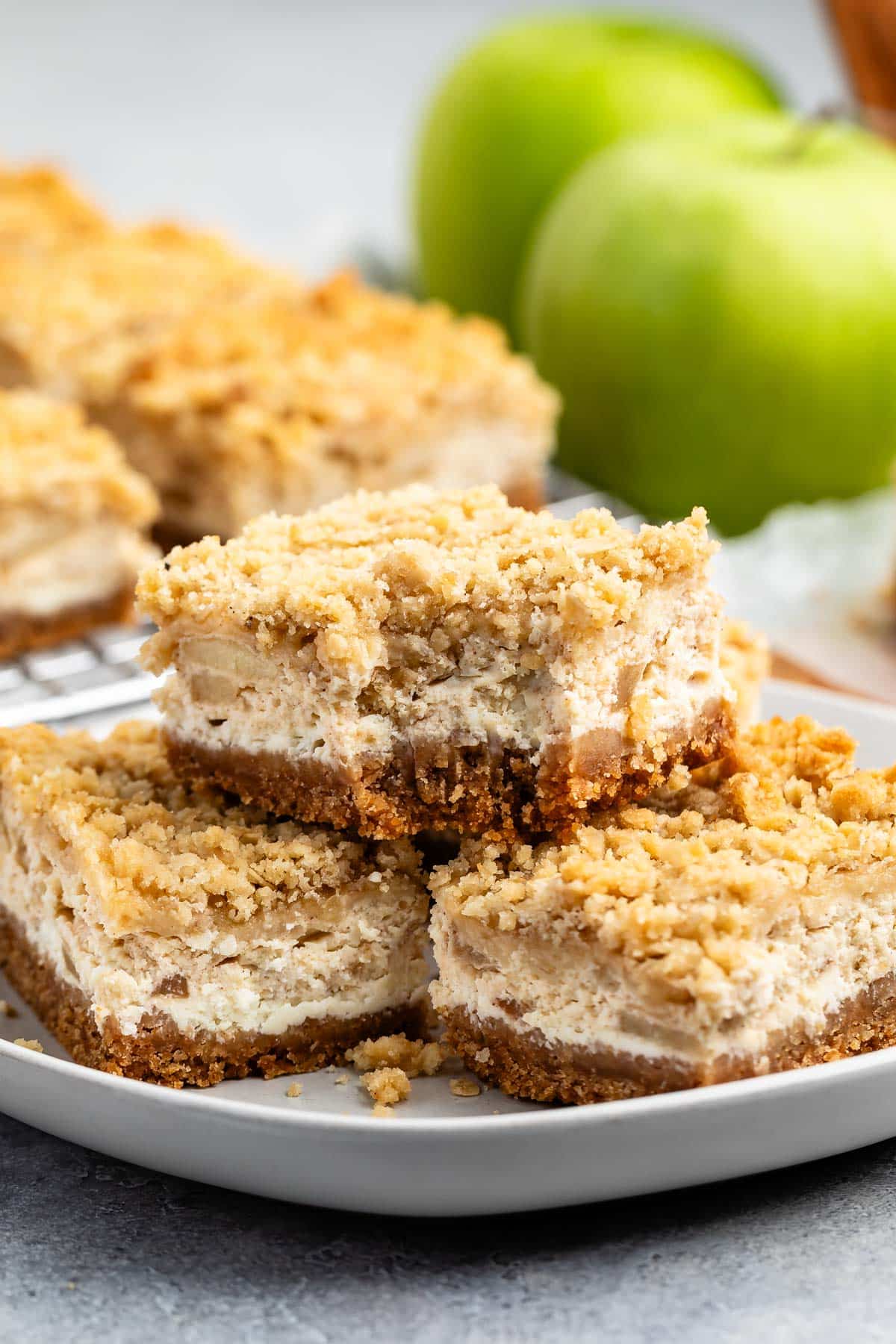 stacked apple cheesecake bars on a grey plate with a crumble topping.