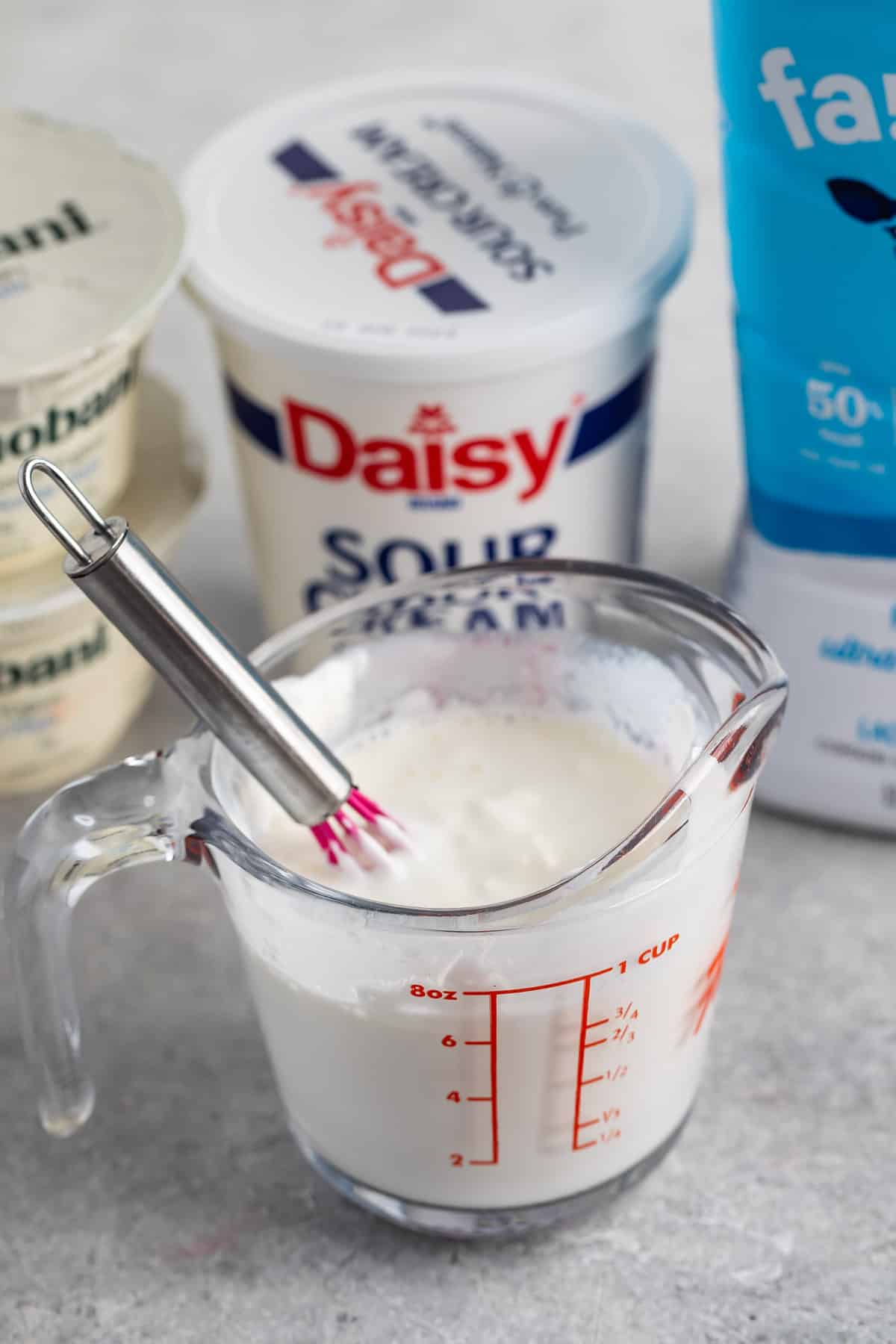 glass measuring cup of buttermilk with a whisk.