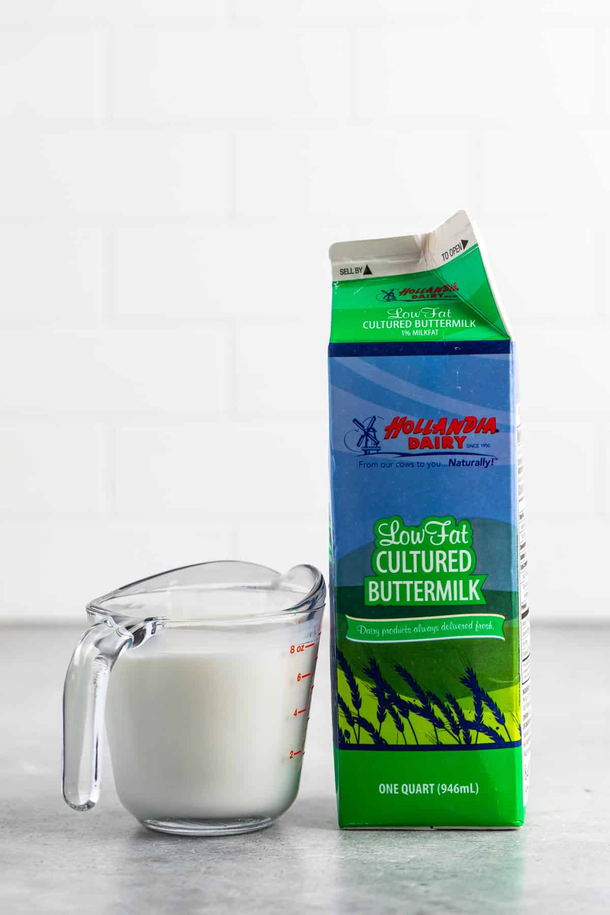 glass measuring cup of milk next to a carton of milk.