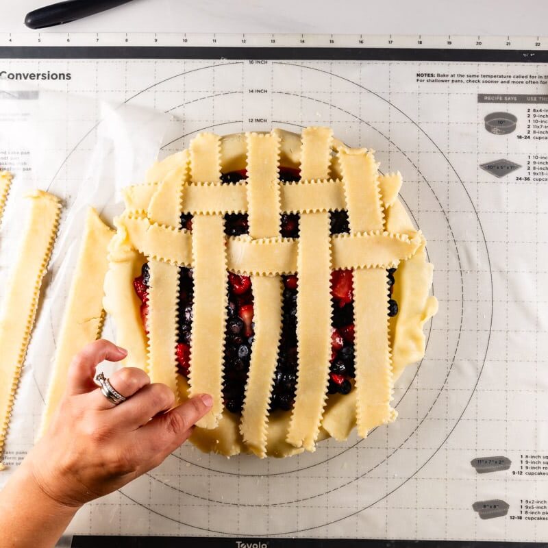 hand making lattice on top of pie.