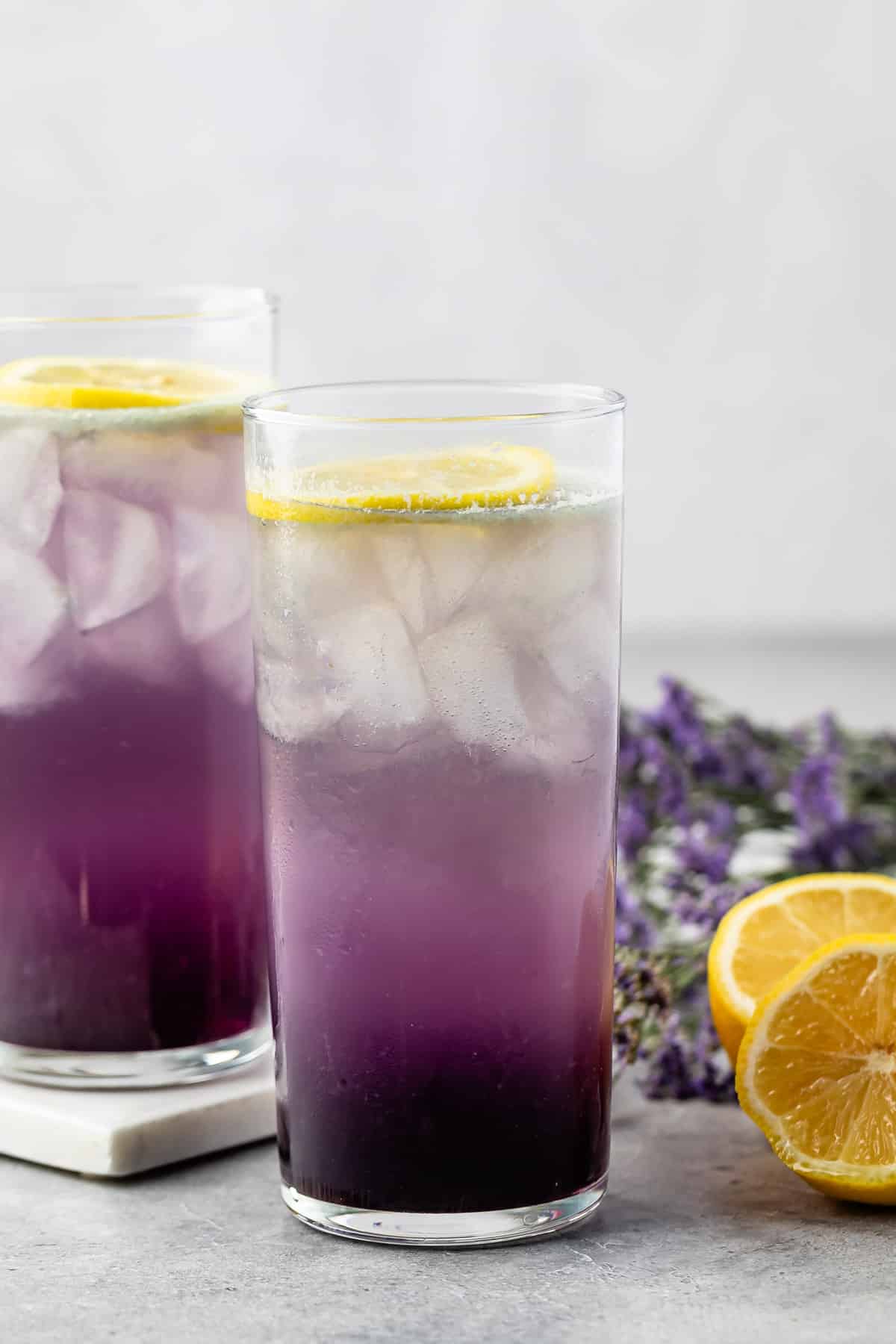 2 tall glasses with purple drink, lemon and lavender behind.