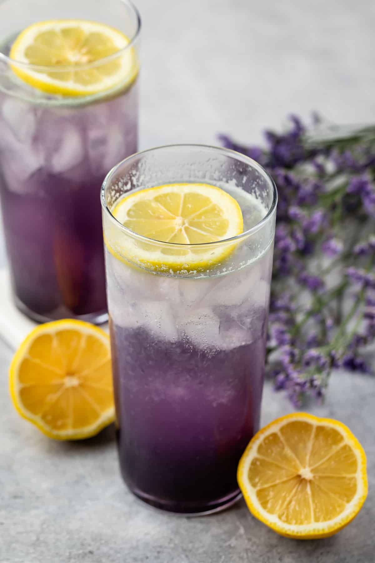 2 tall glasses with purple drink, lemon and lavender behind.