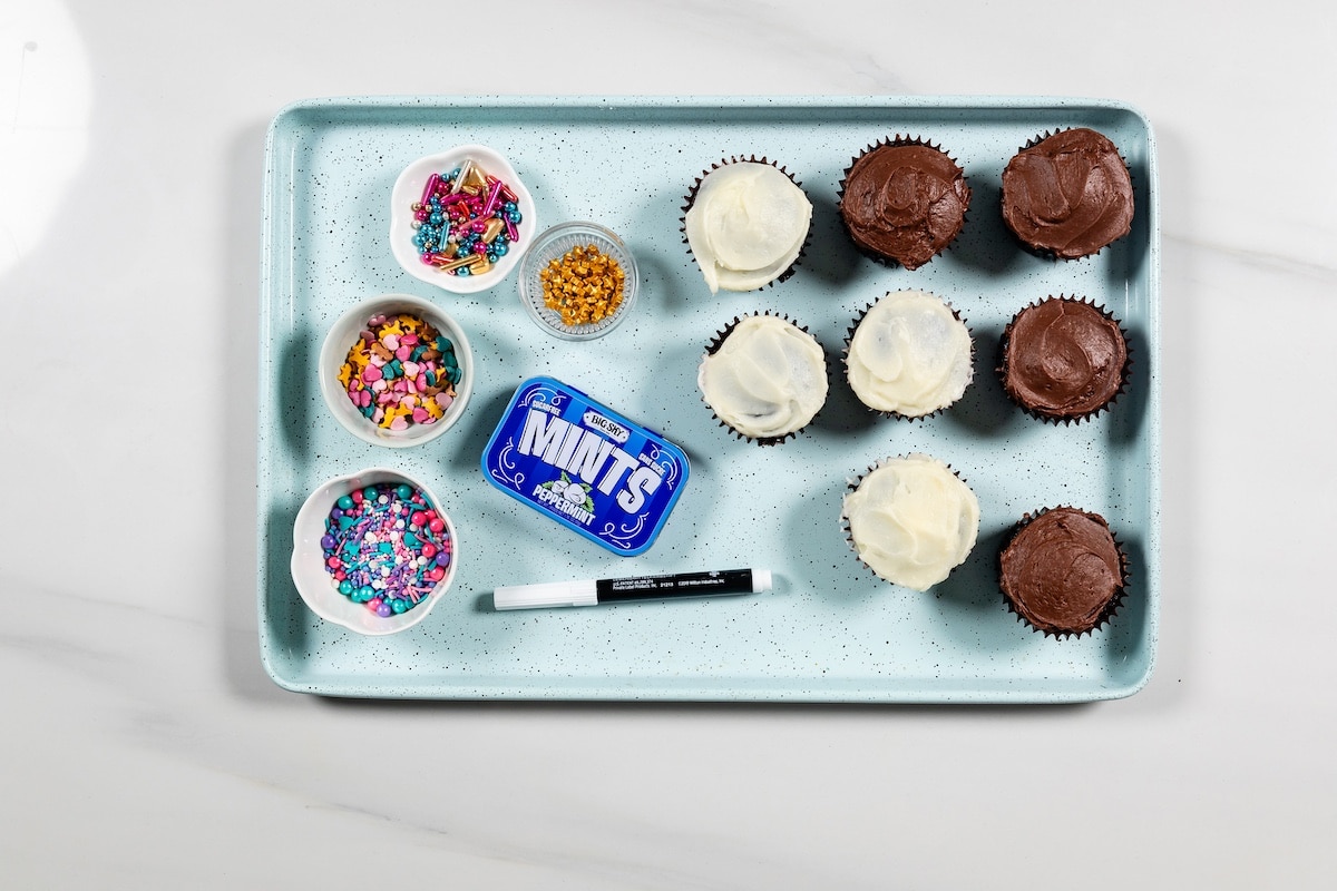 cupcakes, mints, sprinkles, pen on blue cookie sheet.