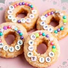 4 doughnuts on pink cake plate with sprinkles and candy.