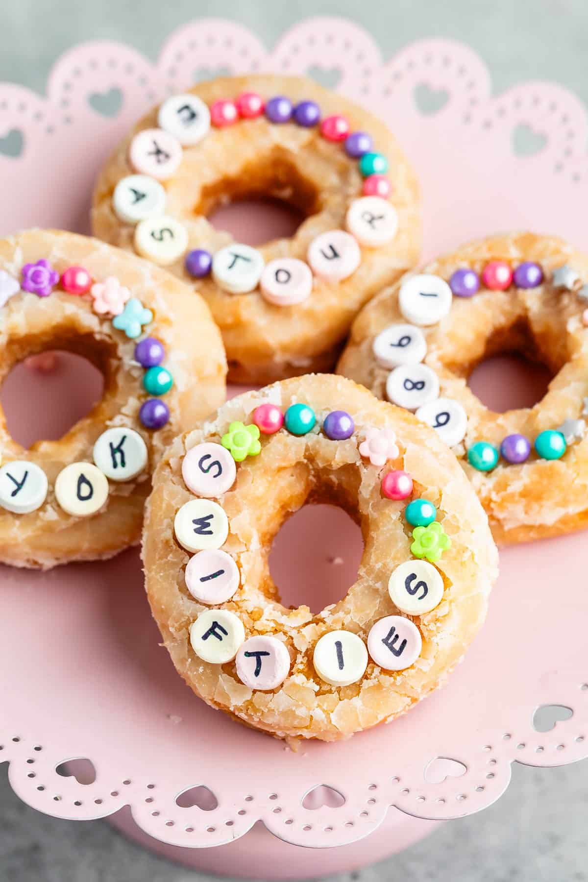 4 doughnuts on pink cake plate with sprinkles and candy.